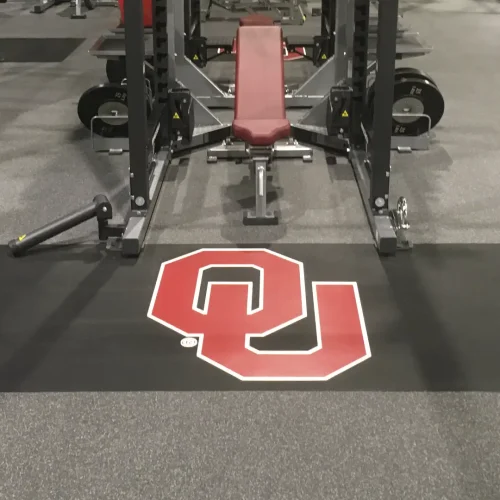 Inlaid OU monogram floor graphic installed on rubber flooring within a collegiate weight room platform