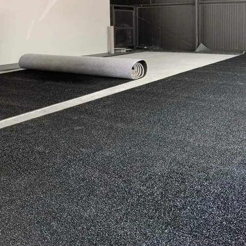 Black turf installation in progress with one roll being unrolled and another section already laid in place.